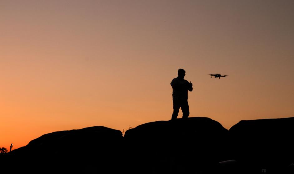 A drone operator and aircraft silhouetted against the evening sky